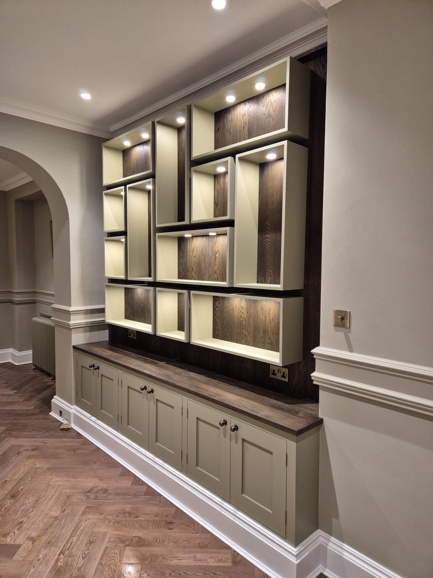 Bespoke illuminated shelving unit with dark walnut recesses and herringbone oak flooring